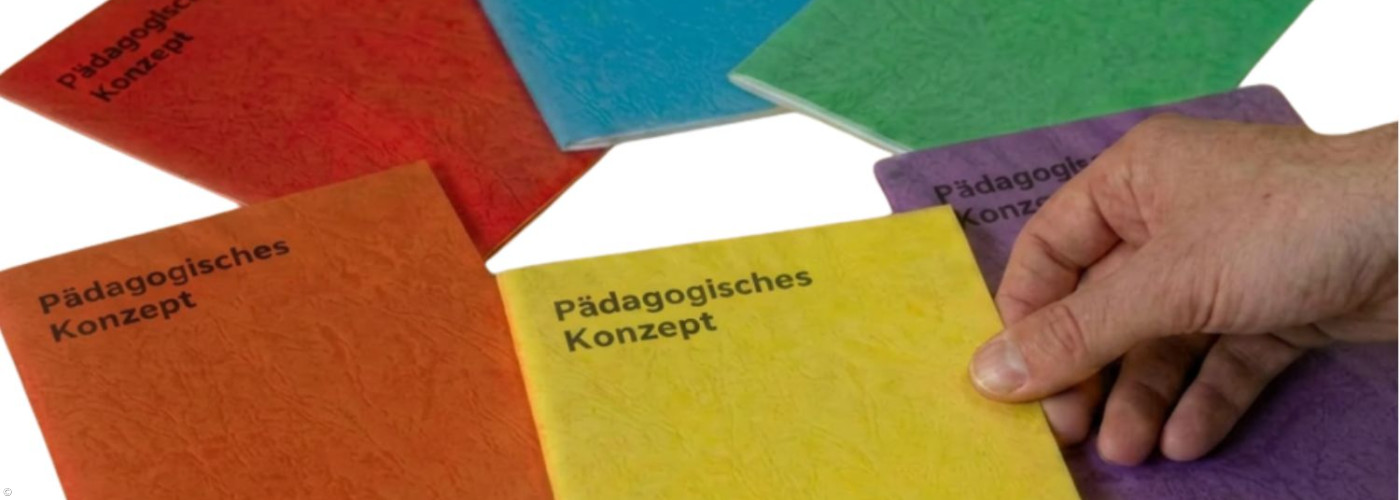 Das Bild zeigt mehrere farbige Broschüren mit dem Titel „Pädagogisches Konzept“, die fächerförmig auf einer hellen Fläche ausgebreitet sind. Die Hefte sind in verschiedenen Farben gehalten, darunter Rot, Blau, Grün, Gelb, Orange und Violett. Im Vordergrund greift eine Hand nach einer gelben Broschüre. In der rechten unteren Ecke ist ein kleines Logo zu sehen.